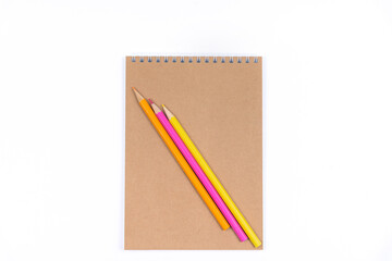 Three colored pencils are on a closed notebook.