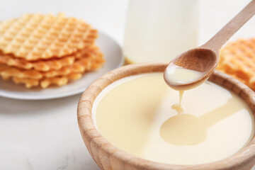 Bowl and spoon with sweet condensed milk on table, closeup