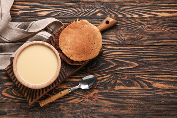 Bowl with sweet condensed milk and pancakes on wooden background