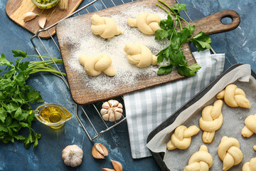 Baking sheet and board with uncooked garlic buns on color background