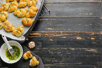 Baking sheet with tasty garlic buns on dark wooden background