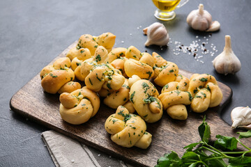 Naklejka premium Freshly baked garlic knots with parsley and olive oil on a wooden board, ready to serve as an appetizer