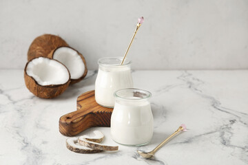 Jars of tasty coconut yogurt on light background