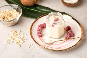 Tasty coconut yogurt with raspberry on light background
