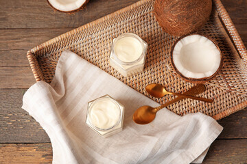 Fototapeta na wymiar Jars of tasty coconut yogurt on wooden background