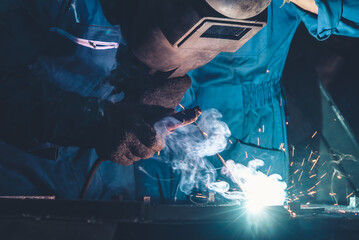 Skillful metal worker working with arc welding machine in factory while wearing safety equipment....