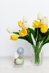 Easter eggs in a glass and a bouquet of flowers in a vase Copy Space