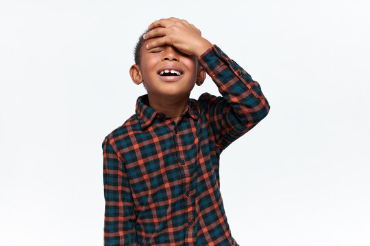Portrait of emotional confused dark skinned little boy in checkered shirt closing eyes, keeping hand on his forehead, making disappointed forgetful facial expression, having focus or memory problem