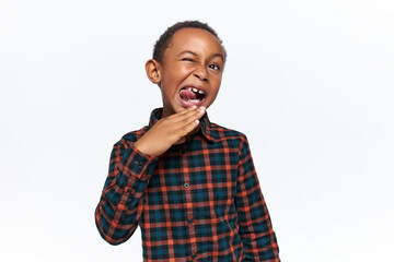 Studio shot of goofy positive dark skinned little boy with milk teeth posing isolated, sticking out...