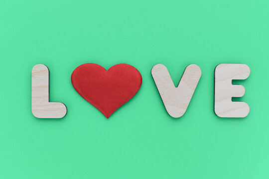 Word LOWE is lined with wooden letters on a green background.
The letter O is replaced with a red heart in the text. Love confession concept. - Powered by Adobe