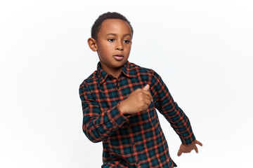 Action shot of adorable active dark skinned little boy wearing casual checkered shirt moving arms as if walking, dancing or doing physical exercises, having confident facial expression