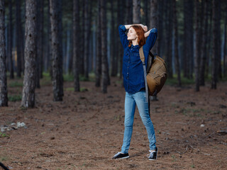 Happy woman having fun in the pine forest with a backpack on her back