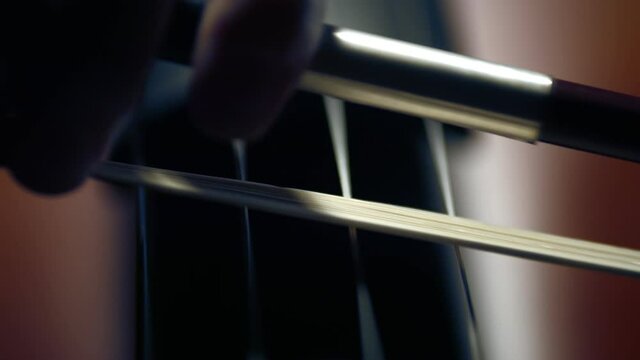 Cello strings and close-up bow in dark light. Playing on cello. Symphony orchestra. Concept of music and musical instruments.