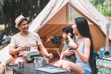 Summer camping in the mountains, spruce forest on background..Back view group of  tourists having a rest together around campfire, enjoying fresh air near tent.happy family on vacation.