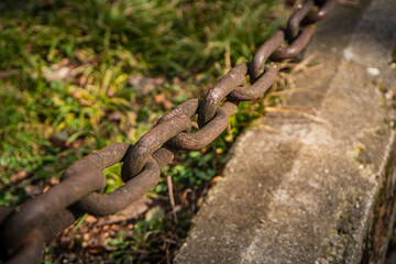 Metal links of a chain, rusty links of a large chain, a fragment of a fence on the background of the earth