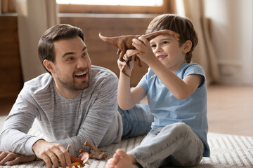 Overjoyed young dad and small 8s son have fun play with animals toys enjoy family weekend at home together. Playful happy Caucasian father engaged in funny game activity with excited little boy child.