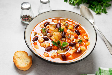 Vegetarian minestrone italian soup made with fresh vegetables, pasta and beans. Light gray background.