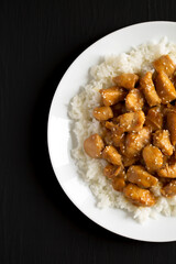 Homemade Orange Chicken with White Rice on a white plate on a black background, top view. Overhead, from above, flat lay. Copy space.