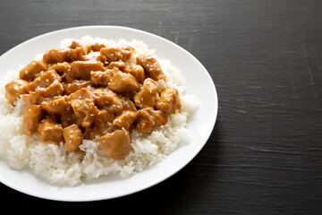 Homemade Orange Chicken with White Rice on a white plate on a black background, side view. Copy space.