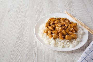Homemade Orange Chicken with White Rice on a white plate on a white wooden background, side view. Space for text.