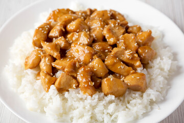Homemade Orange Chicken with White Rice on a white plate on a white wooden background, side view. Close-up.