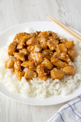 Homemade Orange Chicken with White Rice on a white plate on a white wooden background, side view.