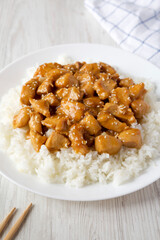 Homemade Orange Chicken with White Rice on a white plate on a white wooden table, side view.