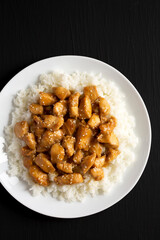 Homemade Orange Chicken with White Rice on a white plate on a black background, top view. Overhead, from above, flat lay. Space for text.