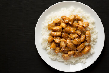 Homemade Orange Chicken with White Rice on a white plate on a black background, top view. Overhead, from above, flat lay. Copy space.