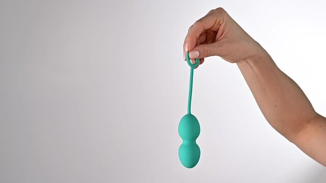 Faceless woman demonstrates a turquoise vaginal ball. Girl holding a kegel trainer for training pelvic floor muscles on a white background.