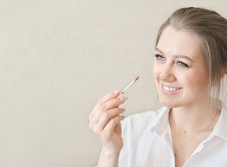 young pretty woman applying concealer on a nose and smiling. perfect skin tone and make up. copy space for text