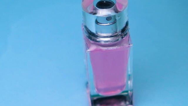 Water flows on a glass thin rectangular bottle with pink perfume on a blue background
