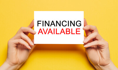 Female hands hold card paper with text Financing Available on a yellow background. Business and...