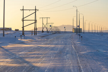 Deserted concrete road in the tundra in the Arctic. Winter sunset view of the road covered with snow and ice. Cold weather. Transport infrastructure in the Far North. Chukotka, Polar Siberia, Russia.