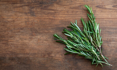 Fototapeta premium Fresh rosemary herb on a wooden background. Top view rosemary with copy space. Cooking concept