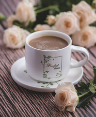 white coffee cup with black coffee, peach roses next to it, everything is on a dark brown wooden table