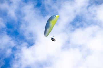 A Paraglider flying into the sky with clouds on a sunny day.