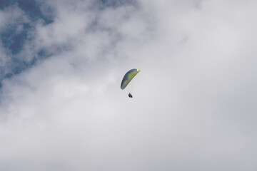 Paraglider flying like a bird in blue cloudy sky.
