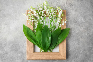 Creative arrangement made with spring lily of the valley flowers in wooden frame on gray concrete...