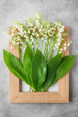 Spring lily of the valley flowers in wooden frame on gray concrete background. Flat lay. Top view. Floral composition