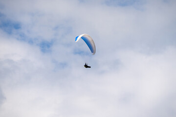 Paraglider flying like a bird in blue cloudy sky.