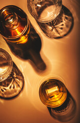 Contemporary still life with whiskey, scotch or bourbon glass with ice on textured brown background with hard lights and shadows, top view, copy space