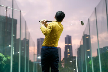 rear view of Asian man practicing golf swing at driving range