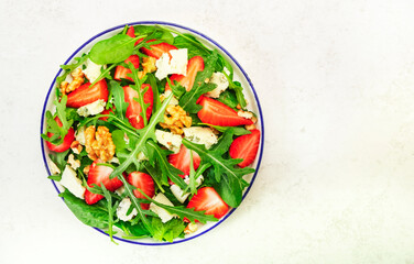 Summer Strawberry Salad. Spinach leaves, arugula, walnuts, blue cheese on gray background. Healthy food concept. Flat lay, top view