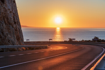 Mountain road without vehicles, curving and with the dawn sun on the horizon over the Mediterranean...