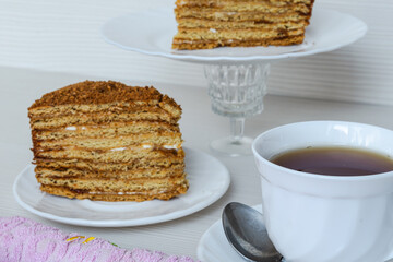 White cup of tea in focus and a piece of honey cake.
