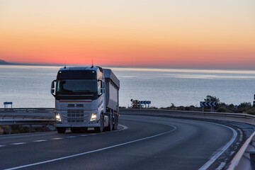 Dump truck on a mountain road by the sea with a sunrise background.