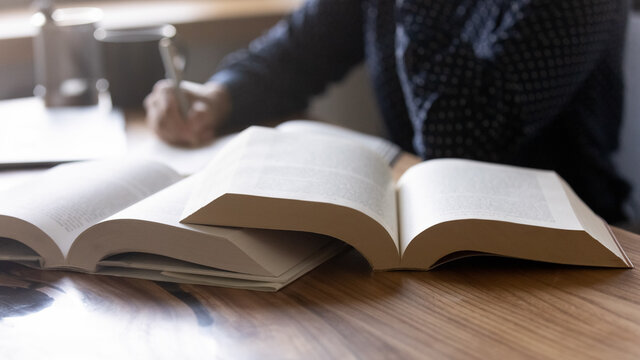 Close up woman student writing notes from textbook, sitting at desk with books, young female preparing for university or college exams, doing homework, school assignments at home, education concept