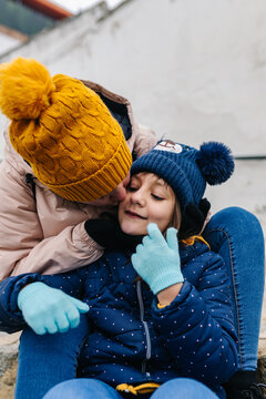 mother giving a complicit kiss to her young daughter on the stairs