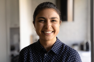 Head shot portrait smiling Indian young woman looking at camera, standing at home, attractive...